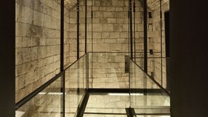 A stone-walled corridor with a glass floor and metal railings. - Palazzo Calò (Bari)
