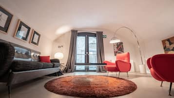 Un salon moderne avec un canapé, un fauteuil rouge, un tapis rond et une grande fenêtre avec des rideaux.