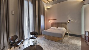 A modern hotel room with a large bed, a small round table, two chairs, a bedside table, and a large window with curtains. - Palazzo Calò (Bari)