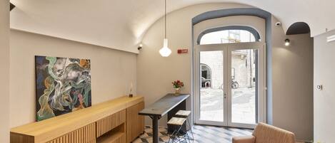 A reception area with a wooden bench, a table, and a sofa. There is a painting on the wall and a door leading outside.