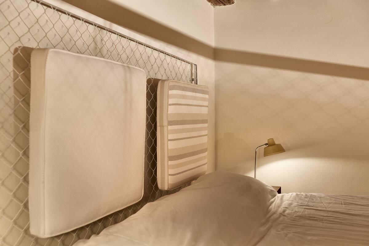 A bed with a headboard, a bedside lamp, and a chain-link fence.
