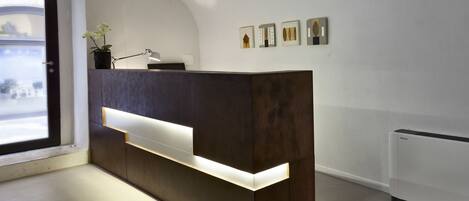 A reception desk with a modern design, a potted plant, and framed botanical prints on the wall.