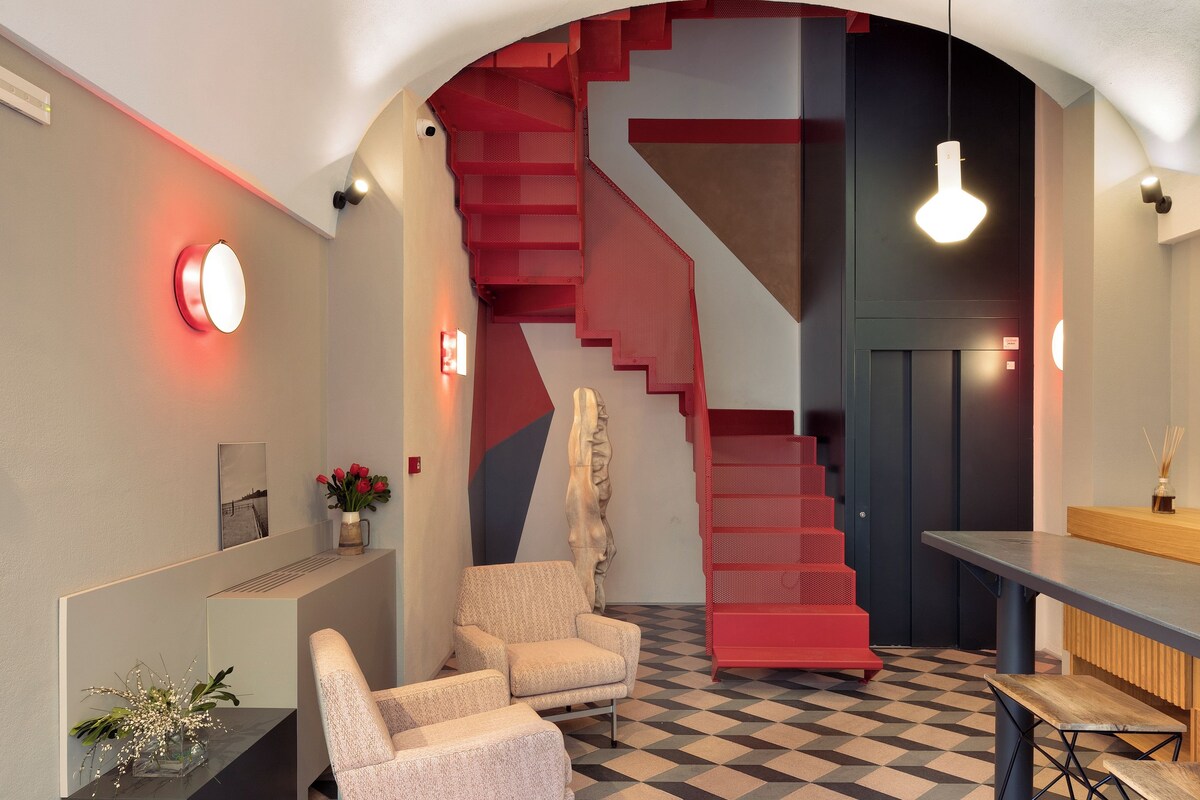 A modern interior with a checkered floor, a staircase with red railings, and a seating area with a table and chairs.