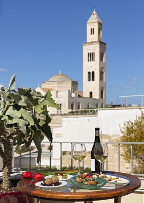 Ein Tisch mit Speisen und Wein auf einem Balkon mit Blick auf einen historischen Turm und eine Kuppel.