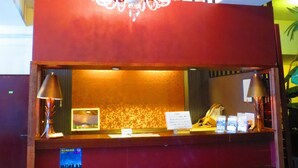A reception desk with a chandelier, a nameplate, and a small window. - Stella Resort - Hostel (Naha)