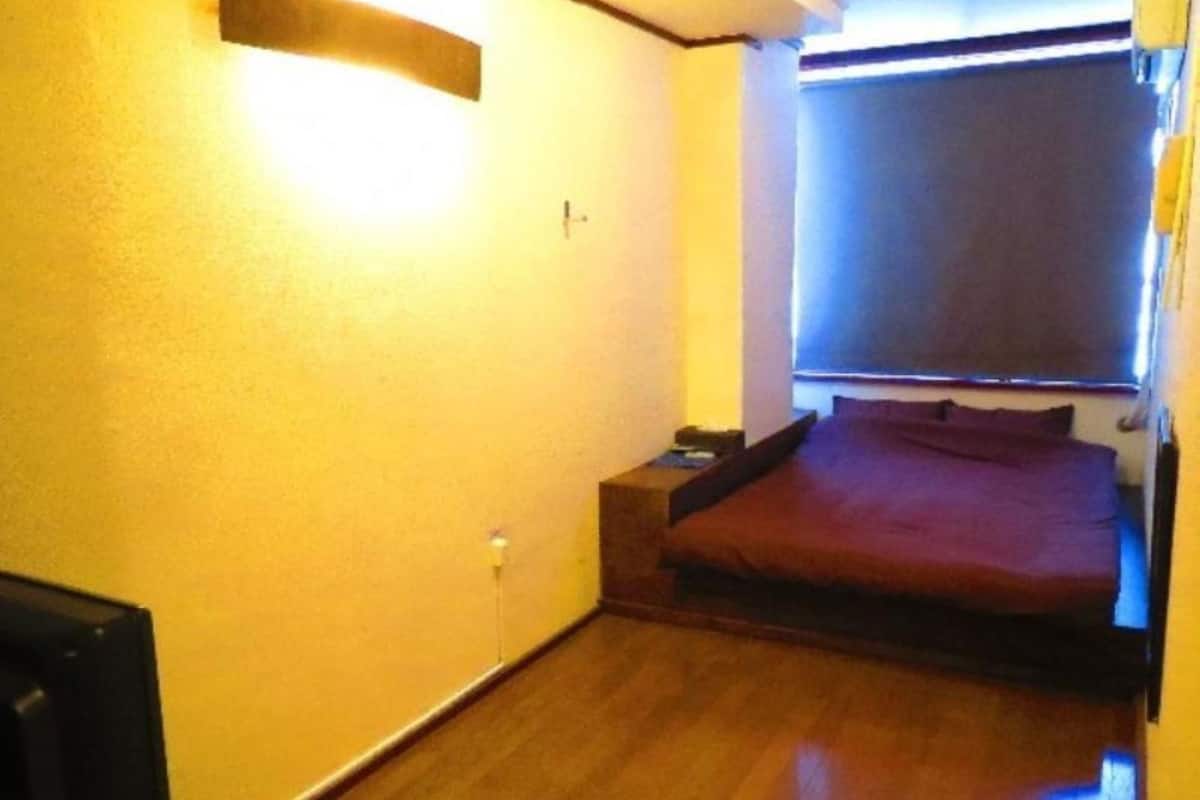 A small, compact room with a single bed, a small table, and a window with blinds.