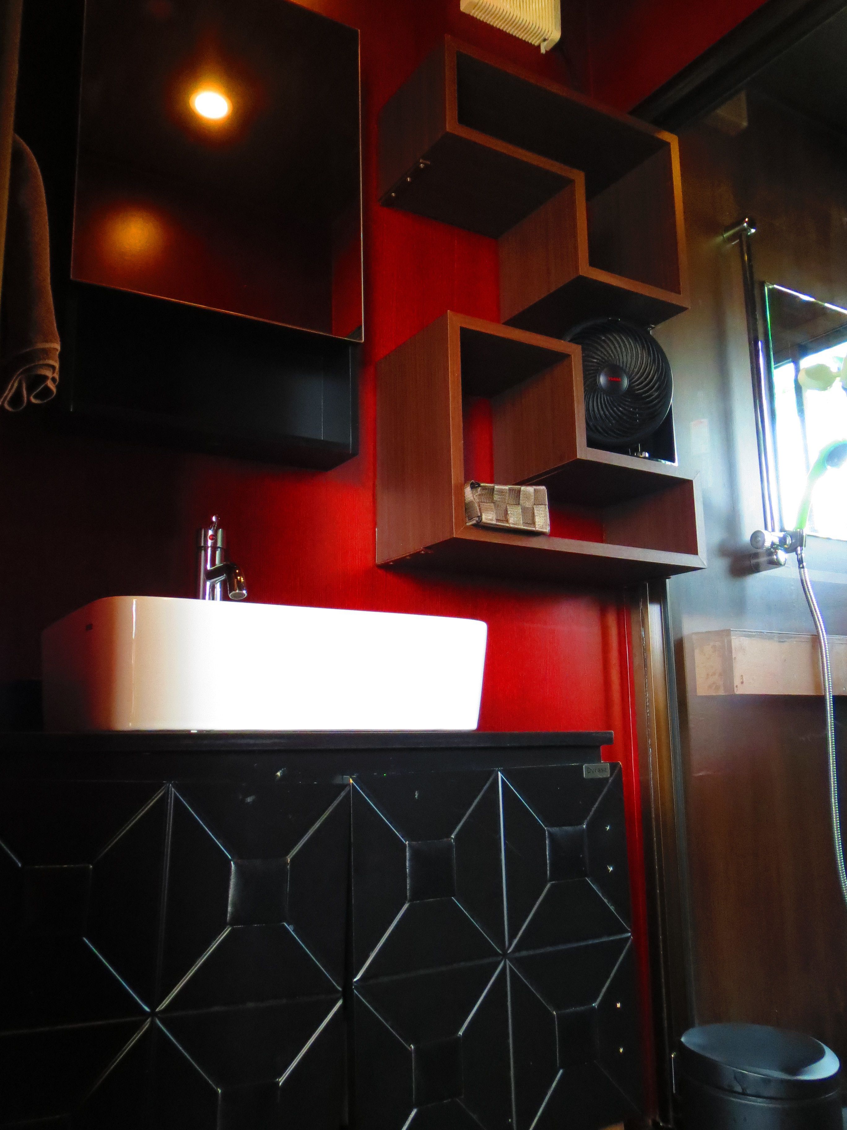 Een badkamer met een witte wastafel, een spiegel en een zwart kastje met geometrische patronen.