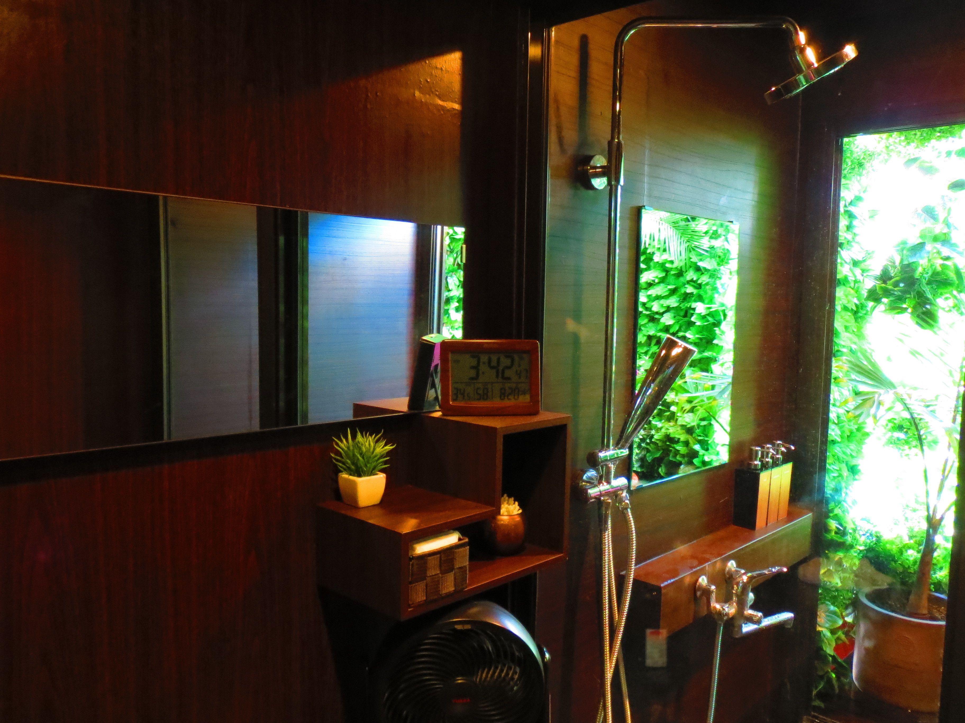 Un baño con tocador de madera, una pequeña planta en maceta, un reloj y una ducha con puerta de vidrio.