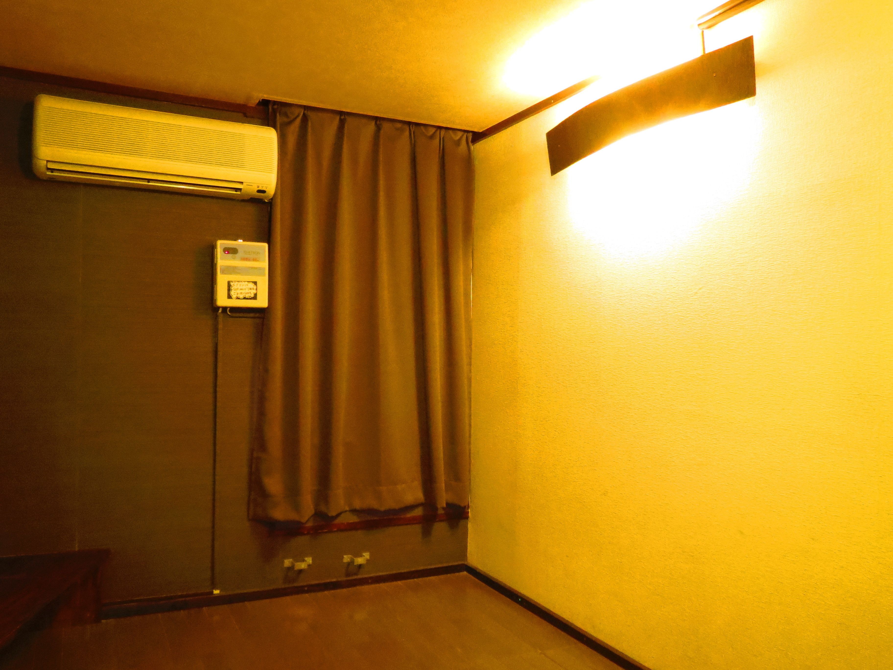 A room with a wall-mounted air conditioner, a door with a curtain, and a light fixture on the wall.
