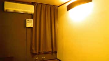 A room with a wall-mounted air conditioner, a door with a curtain, and a light fixture on the wall.