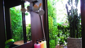 A bathroom with a large mirror, a shower, and a window overlooking a garden. - Stella Resort - Hostel (Naha)