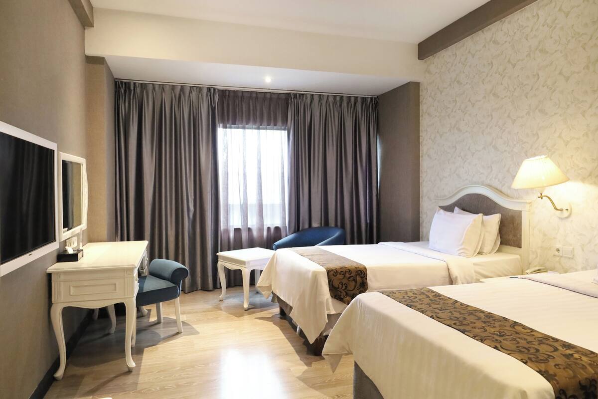 Habitación de hotel con dos camas, un escritorio, una silla, un televisor y una ventana con cortinas.
