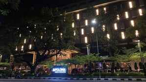 Een hotel met een opvallend verlicht bord, omringd door bomen en geparkeerde auto's.