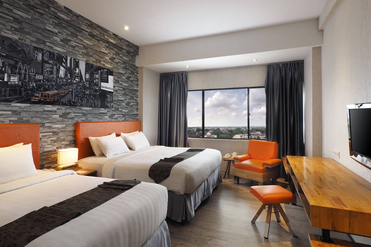 Habitación de hotel con dos camas, un escritorio de madera, una silla, un televisor y un ventanal con vistas a la ciudad.
