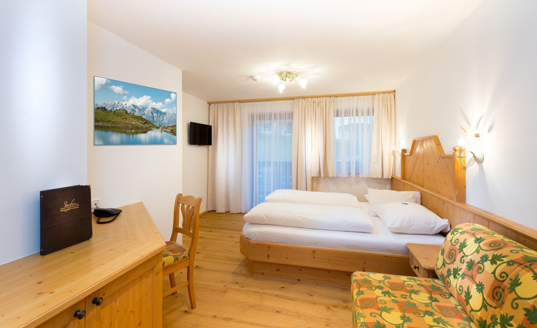 A hotel room with a bed, a desk with a chair, a television, and a window with curtains.