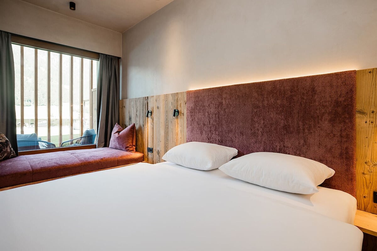A modern bedroom with a large bed, a wooden headboard, and a view of the outdoors through a window.