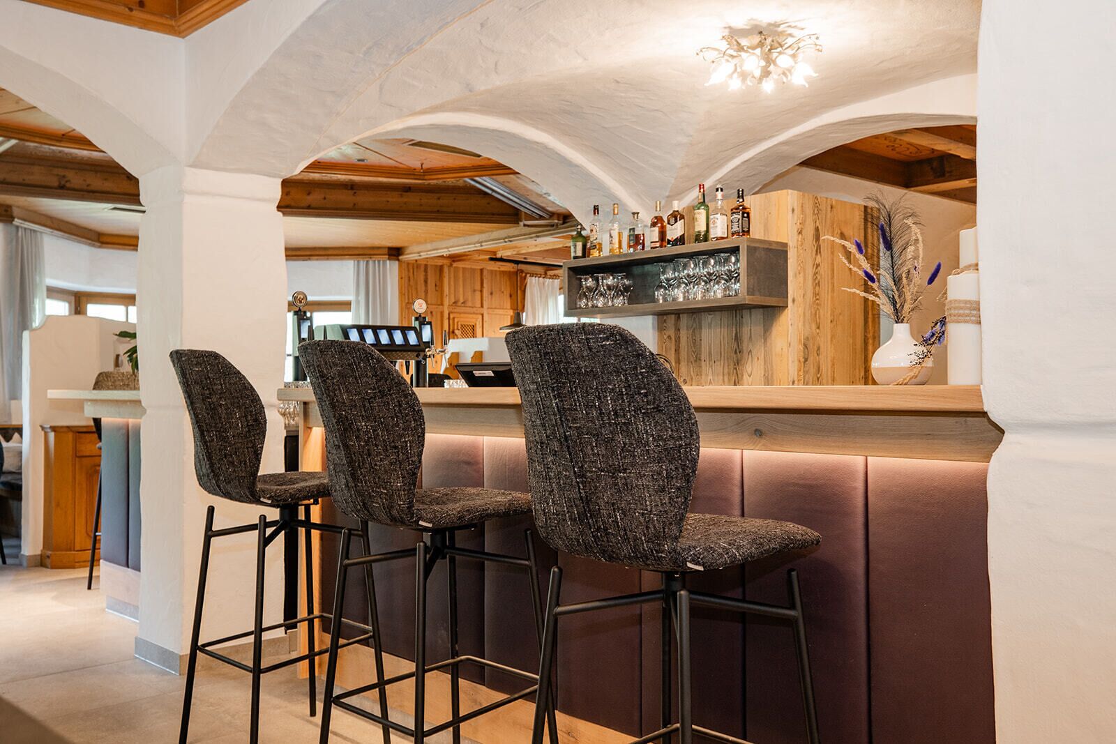 Un espace bar avec quatre tabourets hauts, un comptoir en bois et un assortiment de bouteilles.