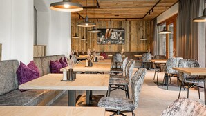 A modern restaurant interior with wooden walls, pendant lighting, and a mix of seating options including tables and sofas. - Hotel Dorfer (Grossarl)