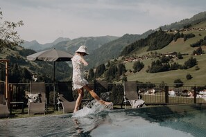A person in a white dress walking on a wet surface near a pool with a mountainous backdrop. - Hotel Dorfer (Grossarl)