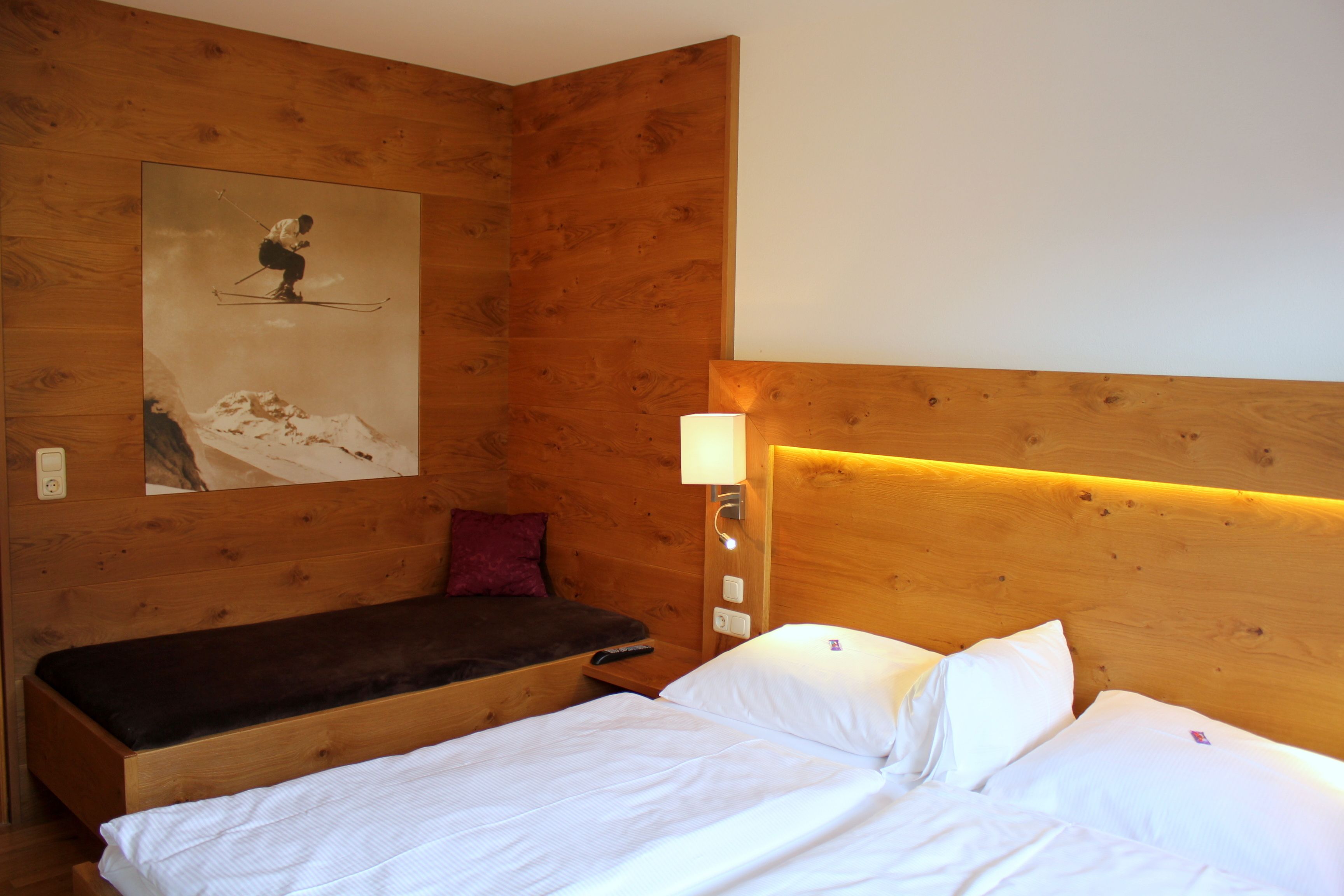 Una habitación de madera con una cama, un banco, una lámpara de pared y un cartel de salto de esquí.