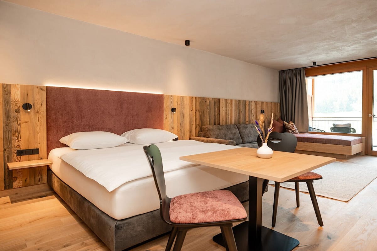 A modern hotel room with a bed, a small table, a chair, and a sofa.