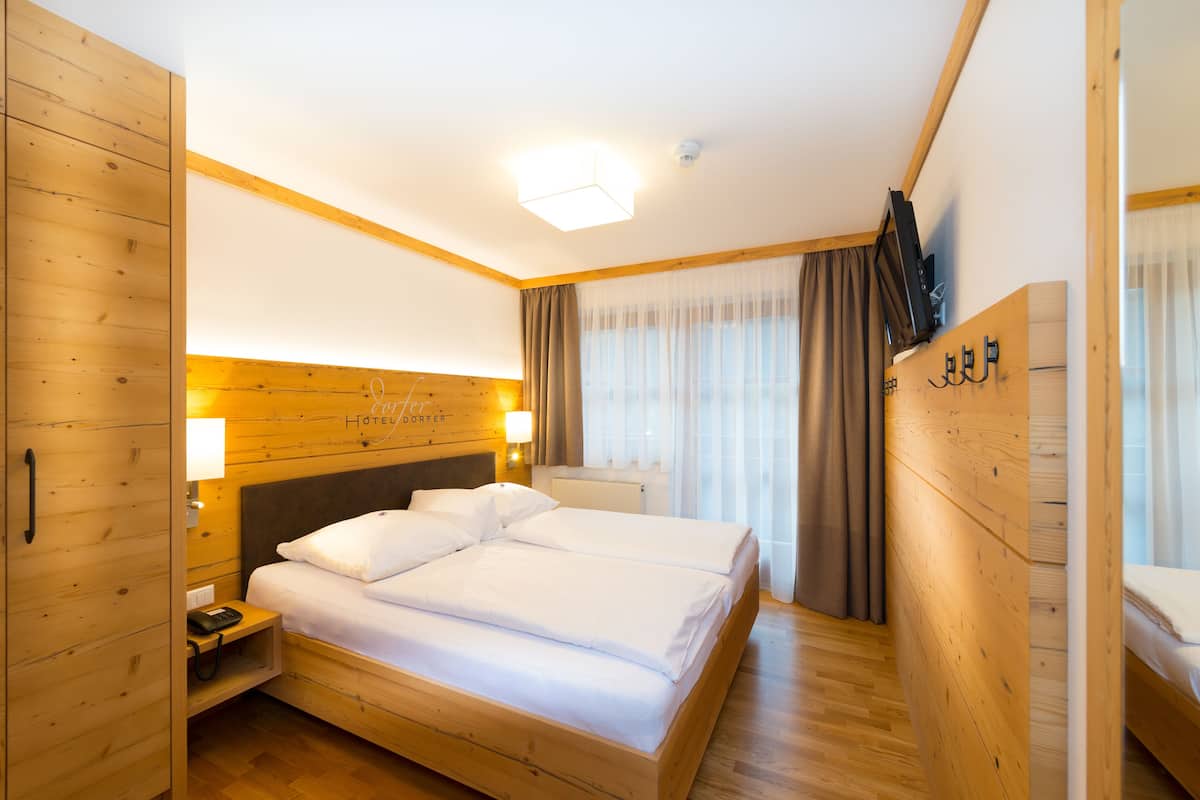 A hotel room with a wooden bed, a nightstand with a phone, a mirror, and a television on the wall.