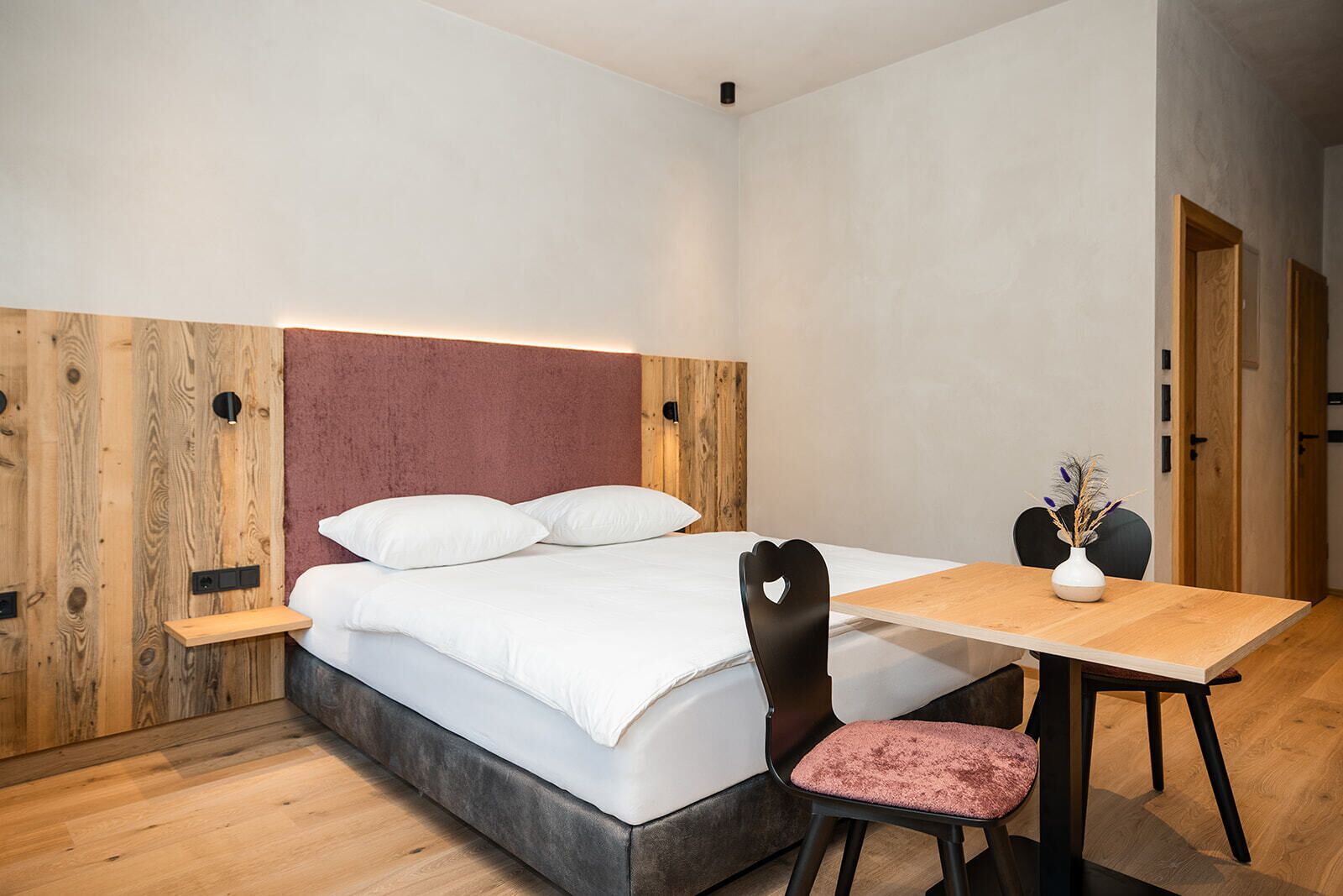 Een moderne slaapkamer met een bed, nachtkastje, stoel en een klein tafeltje met een vaas.
