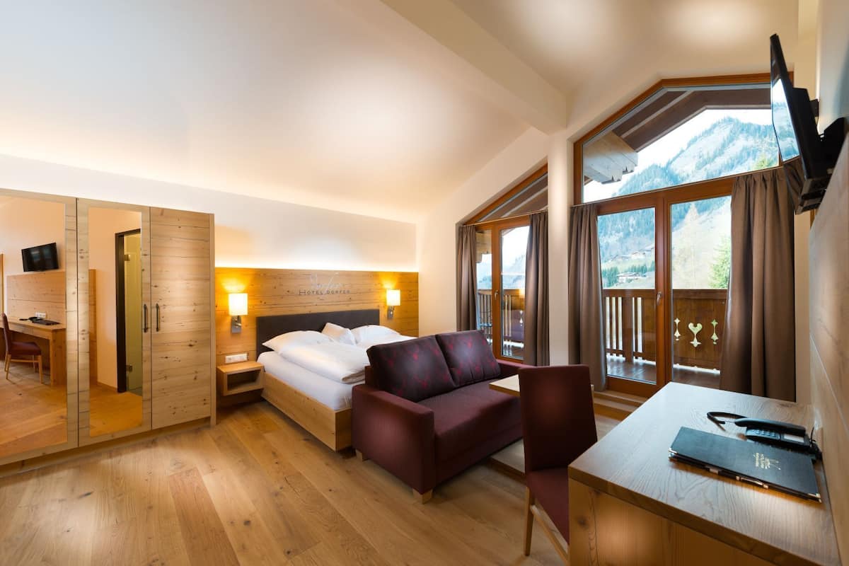 A hotel room with a bed, a desk, a chair, a TV, and a view of mountains through large windows.