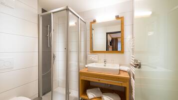Un baño moderno con ducha acristalada, tocador de madera con lavamanos y espejo superior.