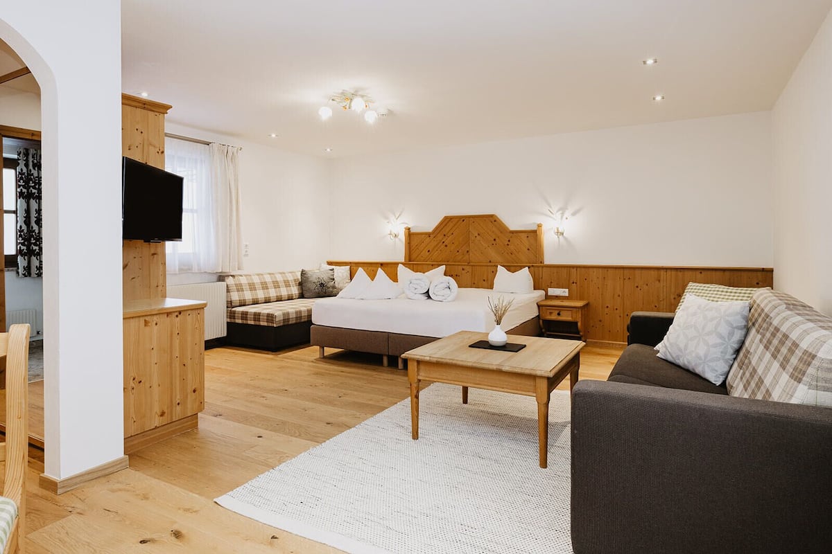 A modern hotel room with a wooden headboard bed, a sofa, a small table, and a TV.