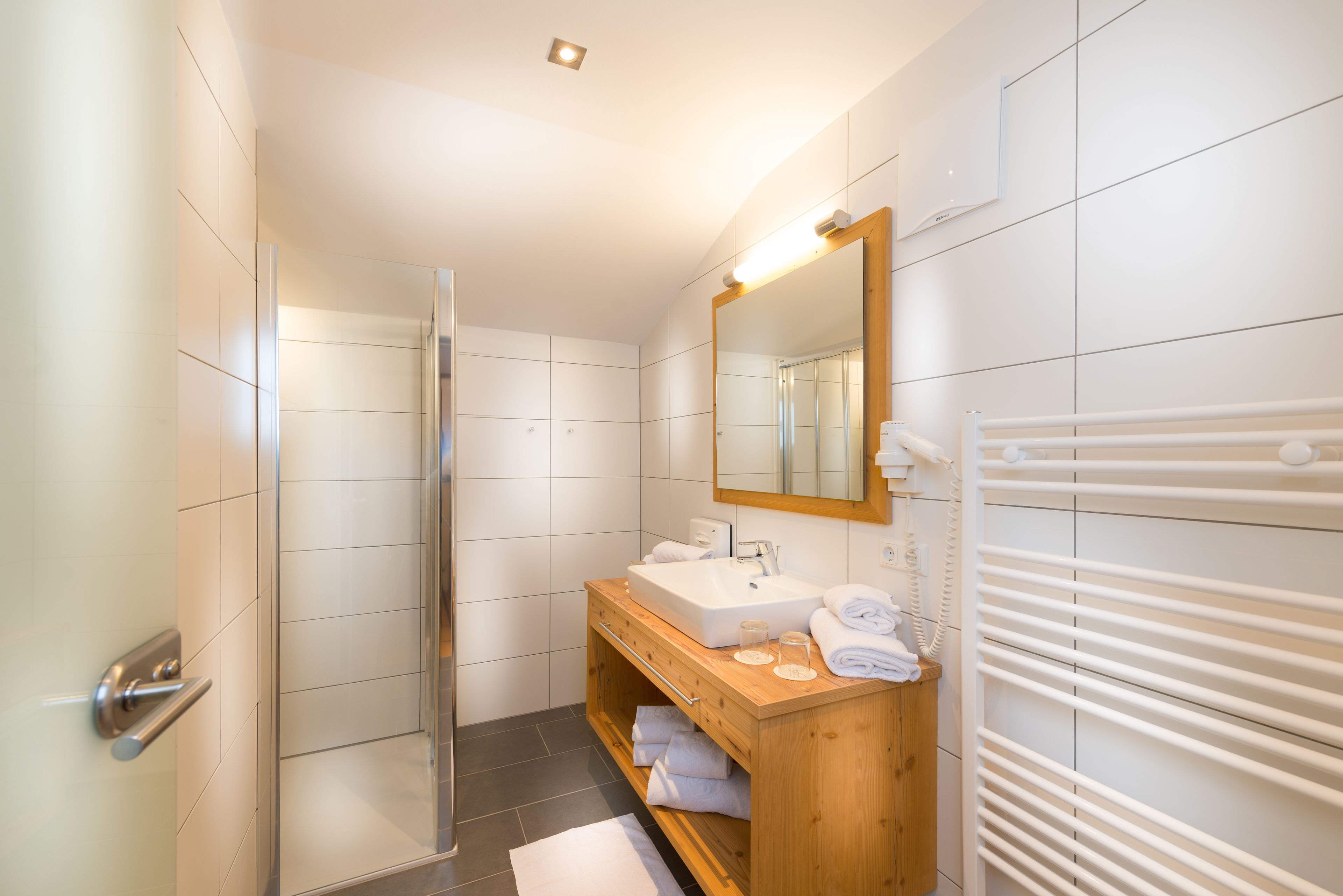 A modern bathroom with a glass shower enclosure, a wooden vanity with a sink, and a towel rack.