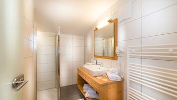 A modern bathroom with a glass shower enclosure, a wooden vanity with a sink, and a towel rack.