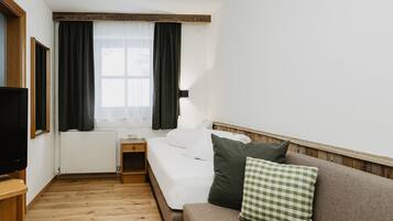 Una habitación de hotel con una cama, una mesita de noche de madera, un televisor, una ventana con cortinas y un radiador.