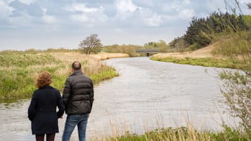 Una pareja caminando a lo largo de la orilla de un río, con un puente al fondo.