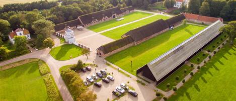 An aerial view of a large estate with multiple buildings, a spacious lawn, and a parking area with several cars.