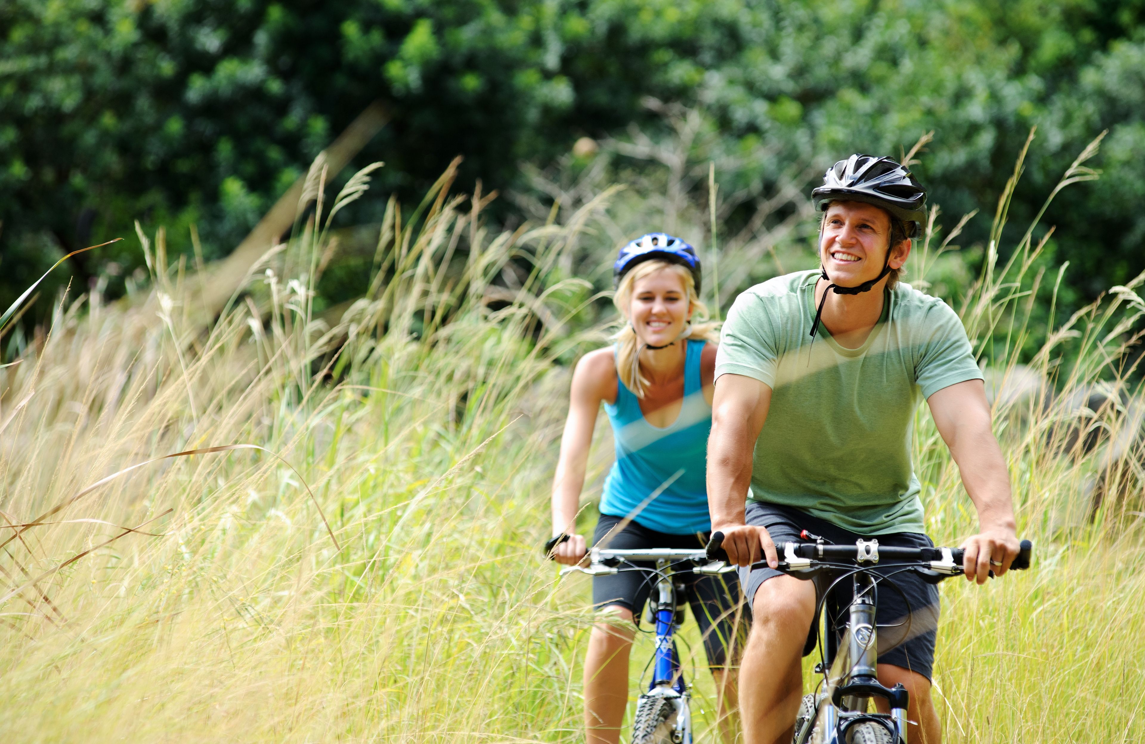 Dos personas paseando en bicicleta por una zona verde con árboles al fondo.