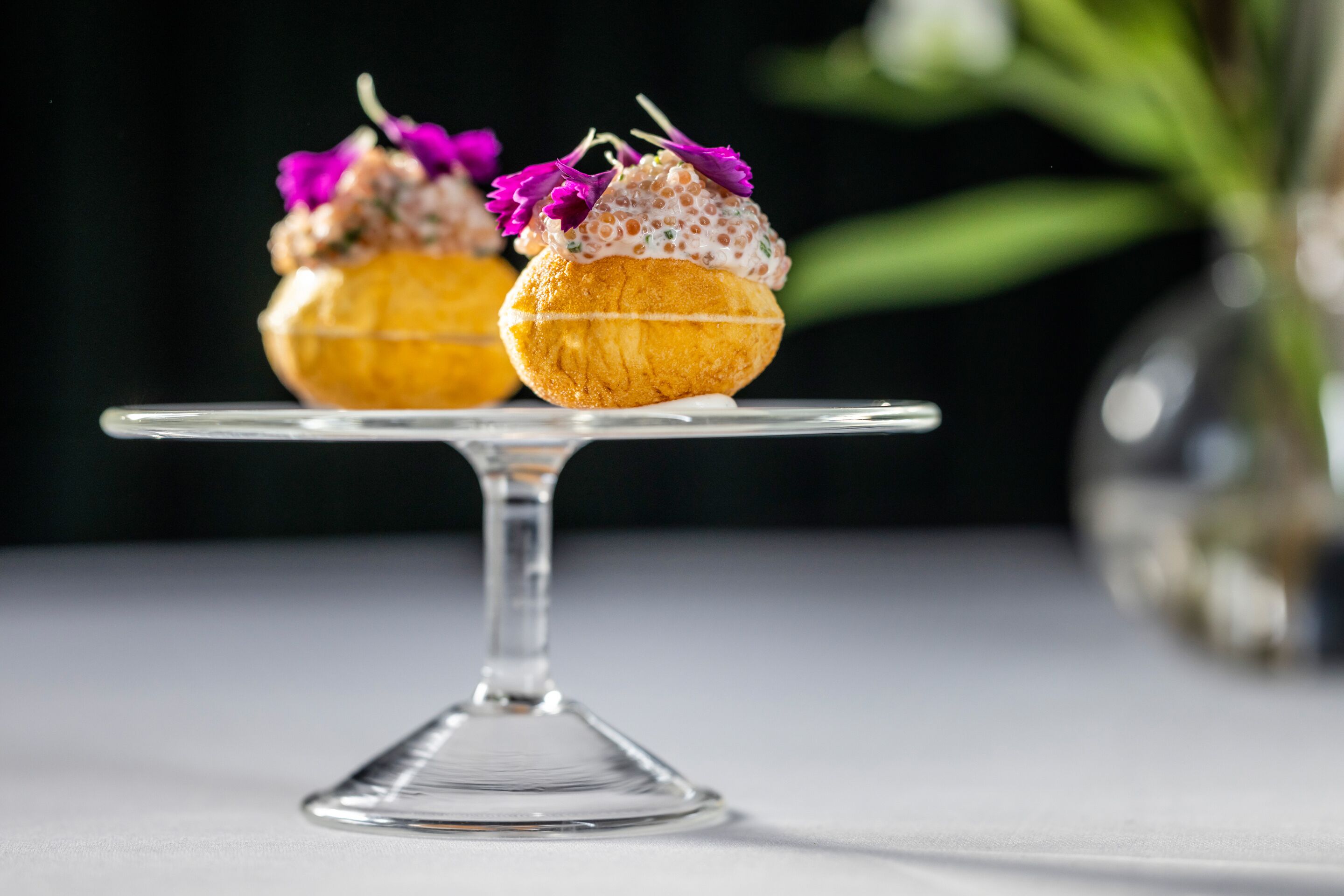 Deux petits gâteaux décorés, présentés sur un présentoir en verre transparent, avec un arrière-plan flou.