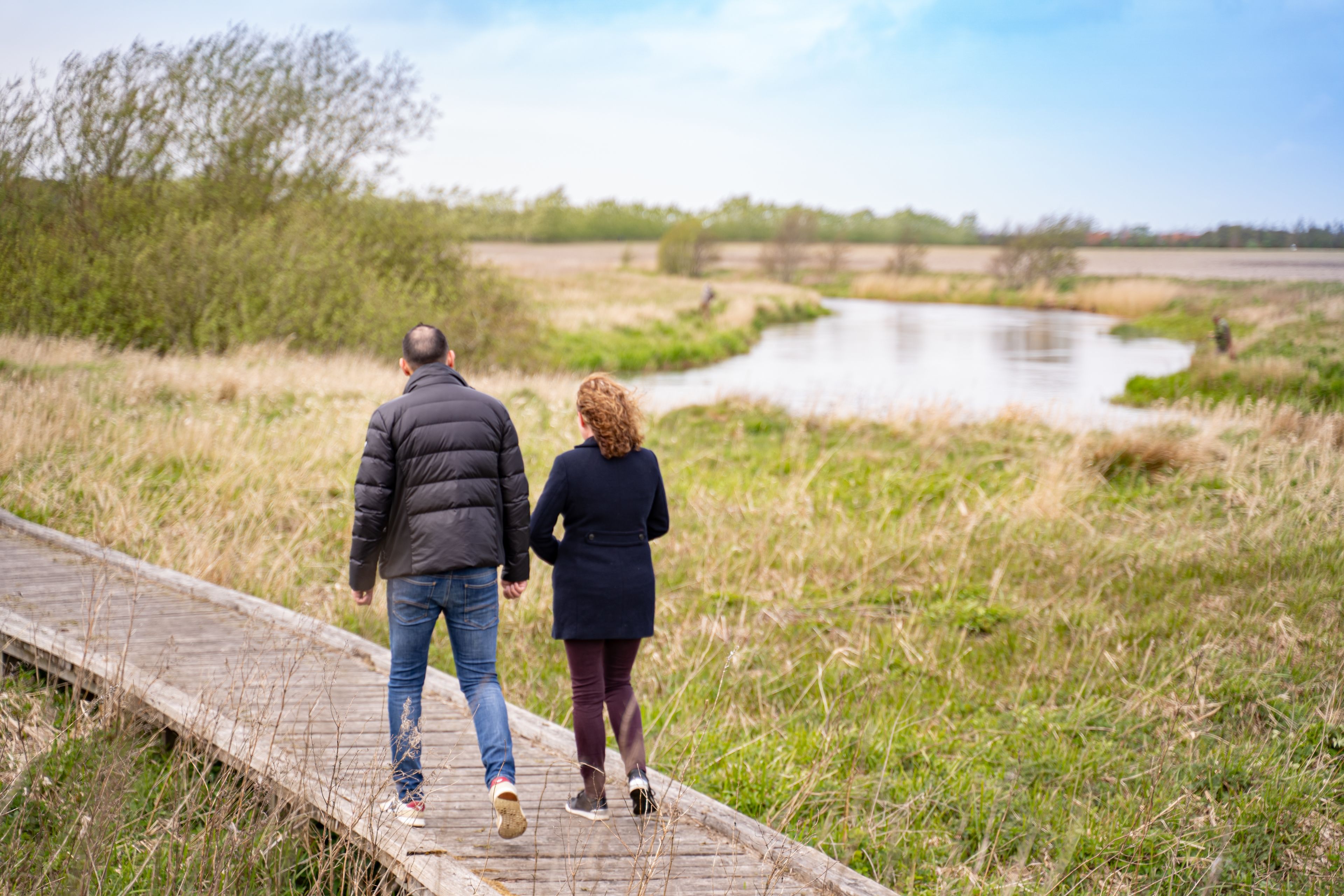A couple walking on a wooden boardwalk beside a river.