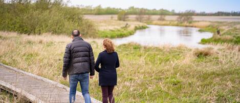 A couple walking on a wooden boardwalk beside a river.