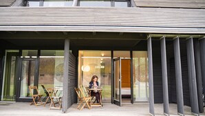 A modern building with a covered entrance, large glass doors, and a seating area with chairs and a table. - Nørre Vosborg Herregård (Vemb)