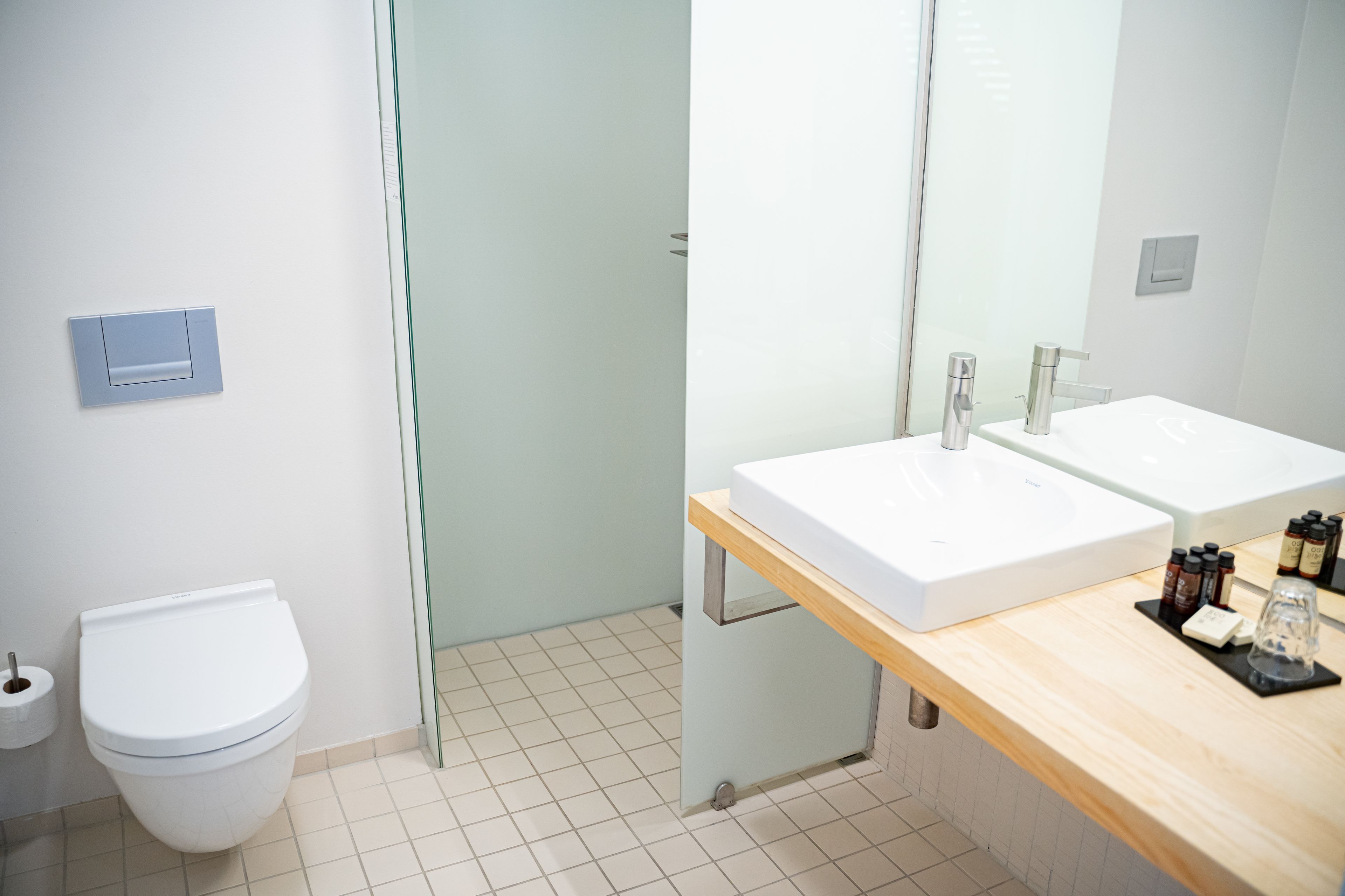 Un baño moderno con inodoro blanco, cabina de ducha de vidrio y tocador de madera con dos lavamanos.