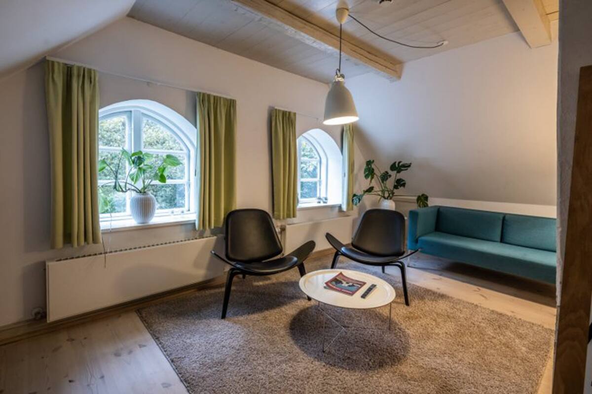 Un salon moderne avec deux fauteuils noirs, une table basse ronde, un canapé de couleur turquoise et un luminaire suspendu.