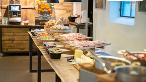 A buffet setup with various food items and utensils on a long table, set in a room with wooden walls and a window. - Nørre Vosborg Herregård (Vemb)