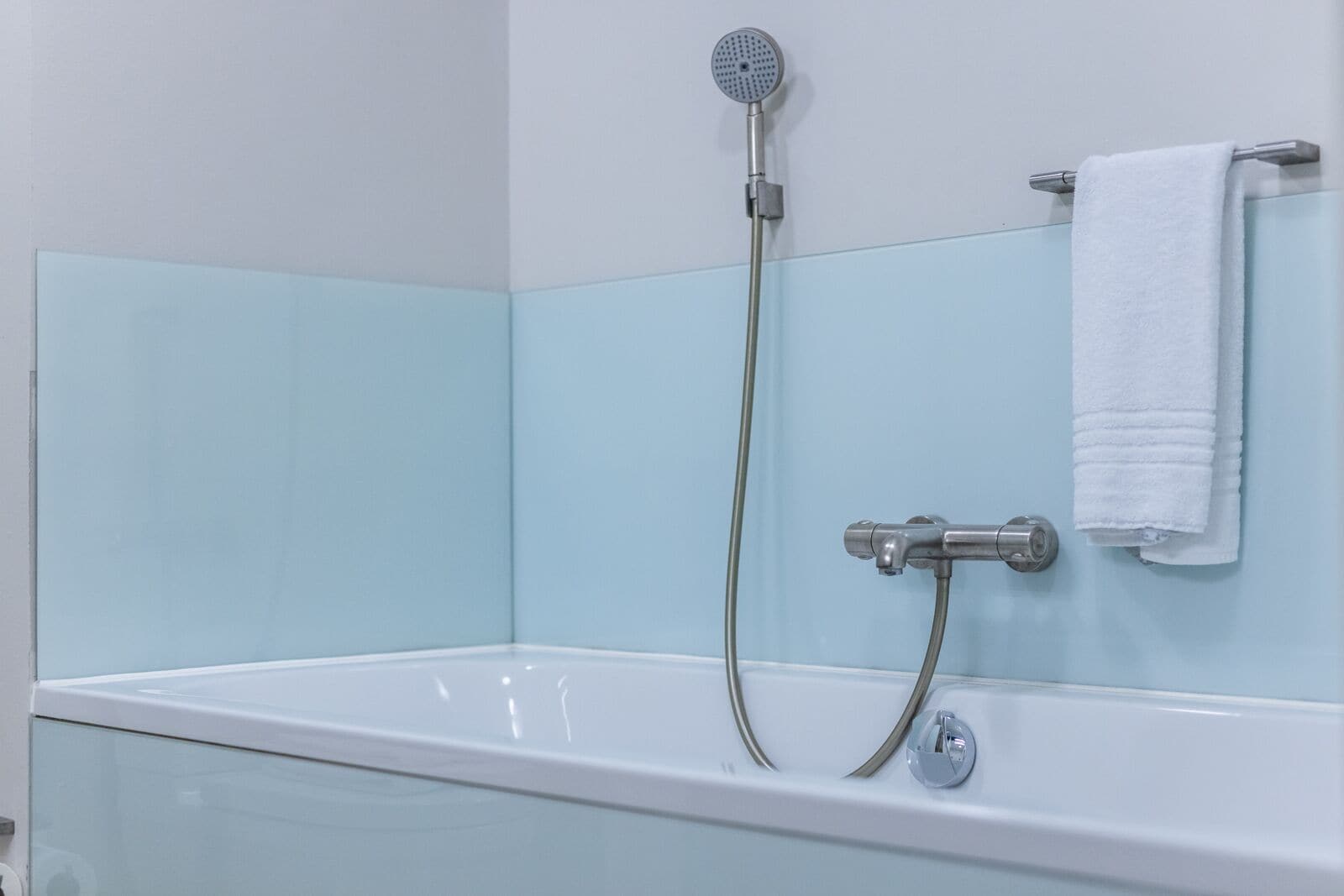 Une salle de bain avec une baignoire blanche, une douchette à main et un porte-serviettes.