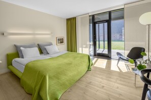 Un dormitorio moderno con una cama grande, una manta verde y vistas al exterior a través de un ventanal corredero.