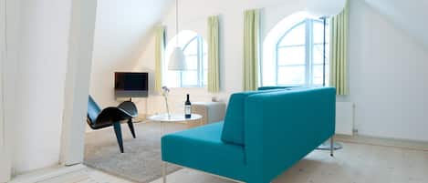 Una sala moderna con un sofá color turquesa, una silla negra, una mesita redonda y un televisor.
