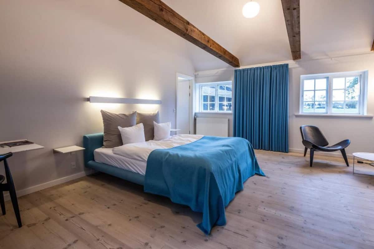 Une chambre à coucher avec un lit, un bureau, une chaise et une fenêtre avec des rideaux.