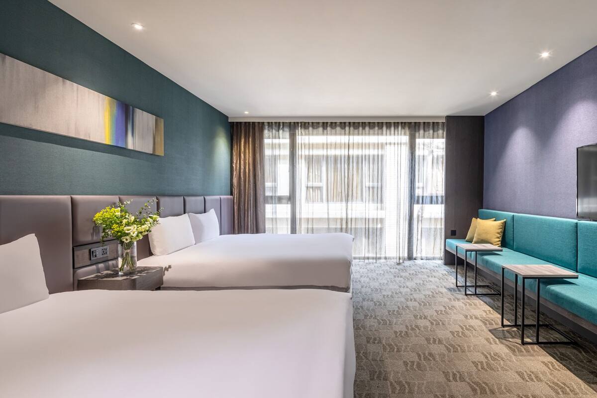 A hotel room with two beds, a sofa, a TV, and a large window with curtains.
