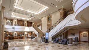 Um hall espaçoso com uma escadaria imponente, pisos de mármore polido e luminárias elegantes.
