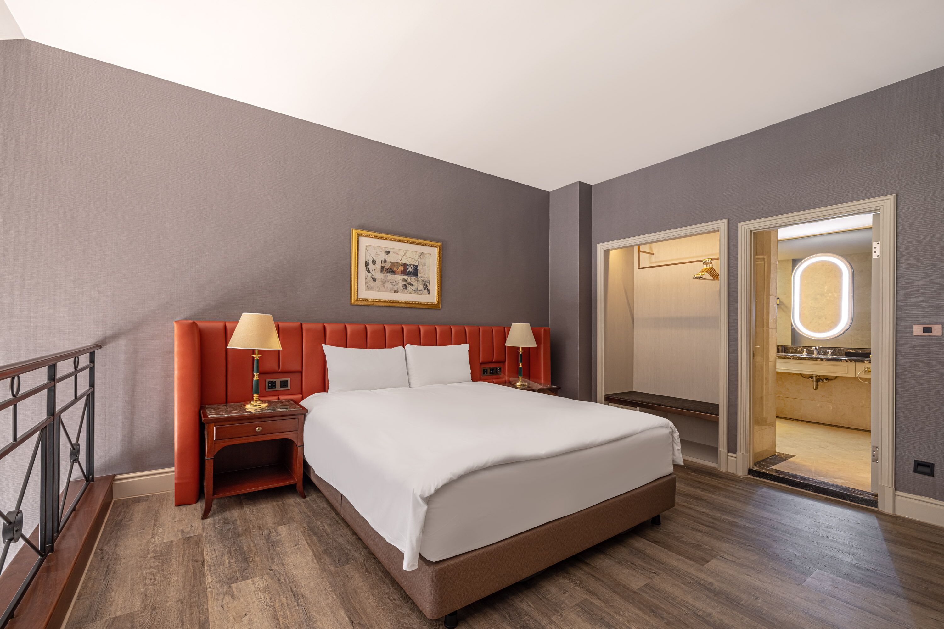 A hotel room with a large bed, a nightstand with a lamp, a framed picture on the wall, and a bathroom visible through an open door.